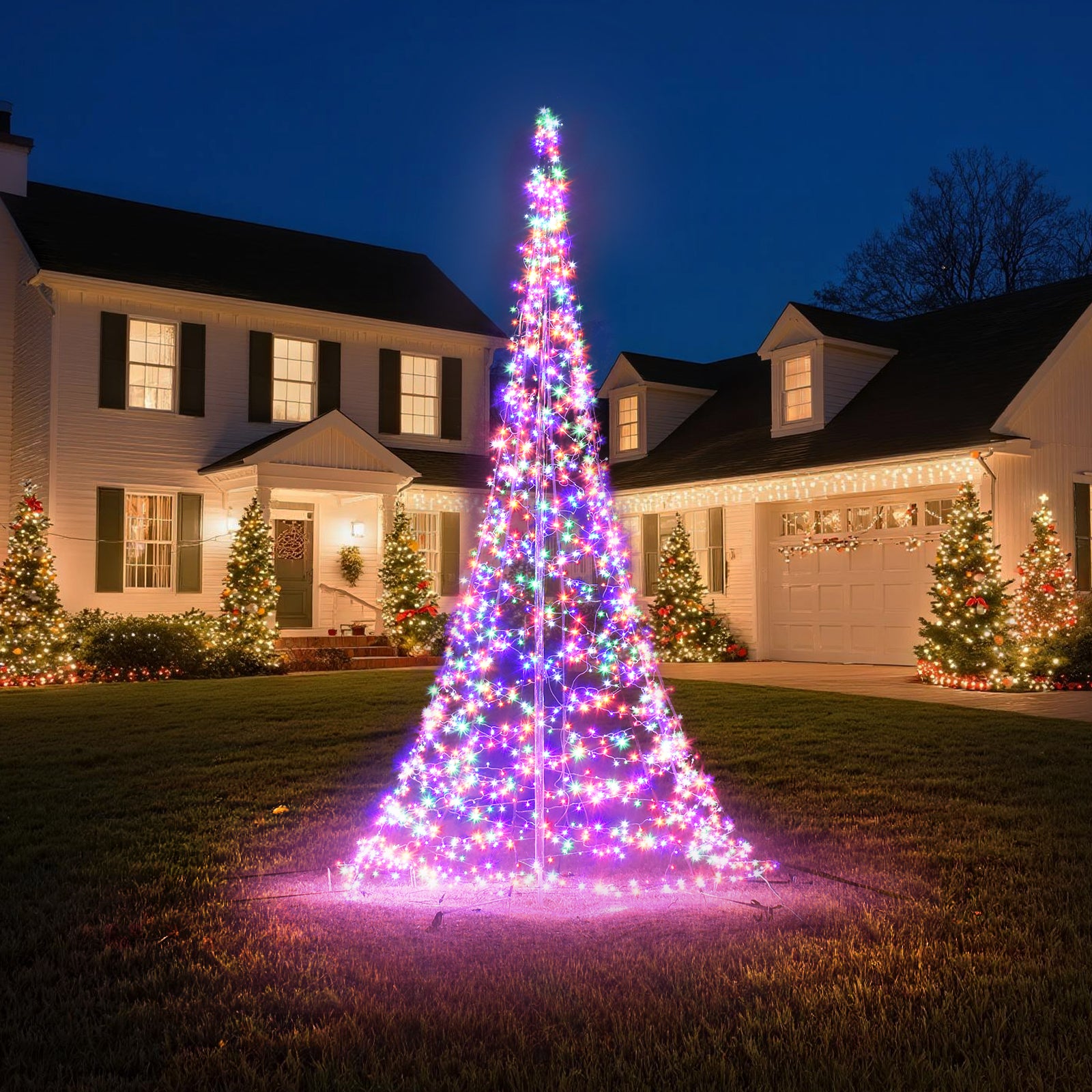 Sapin de Noël multicolore sur mât HOYECHI sur une pelouse, devant des lumières de maison à l’aspect chaud