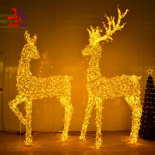 Man standing beside HOYECHI life-size LED buck and doe Christmas deer sculptures showing scale for commercial displays