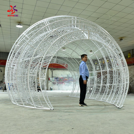 Unlit steel frame of HOYECHI Christmas ball arch with man standing inside showing scale of walk-through LED ornament arch
